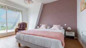 Une chambre à coucher avec un grand lit, une chaise, une table de chevet et une fenêtre donnant sur un beau paysage.