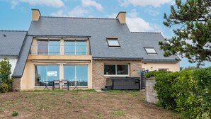 Une maison moderne à deux étages, dotée d’un toit en pente, de grandes fenêtres et d’un espace extérieur aménagé pour se détendre.