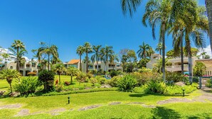 A hotel courtyard with palm trees, a swimming pool, and a well-maintained lawn. - Spacious Wailea Maui Condo with Pool & Tropical Garden Setting (Wailea)