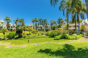 A hotel courtyard with palm trees, a swimming pool, and a well-maintained lawn. - Spacious Wailea Maui Condo with Pool & Tropical Garden Setting (Wailea)