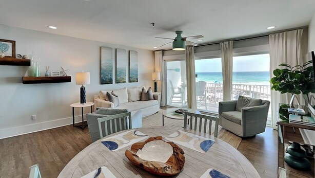 A modern living room with a round coffee table, a sofa, and a chair. There are two side tables with lamps, a ceiling fan, and a large window with a view of the beach. - Luxe Gulf Front Condo, Stunning Views. Community Pool (Santa Rosa Beach)