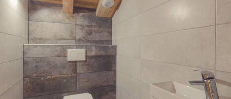 Un baño con techo de madera, un inodoro, un lavabo y una lámpara de pared.