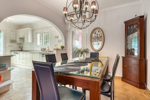 A modern kitchen with white cabinets, a dining area with a glass table, and a chandelier.