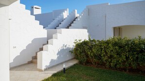 Un bâtiment blanc avec un escalier menant à un étage supérieur, un petit jardin et un ciel bleu dégagé.