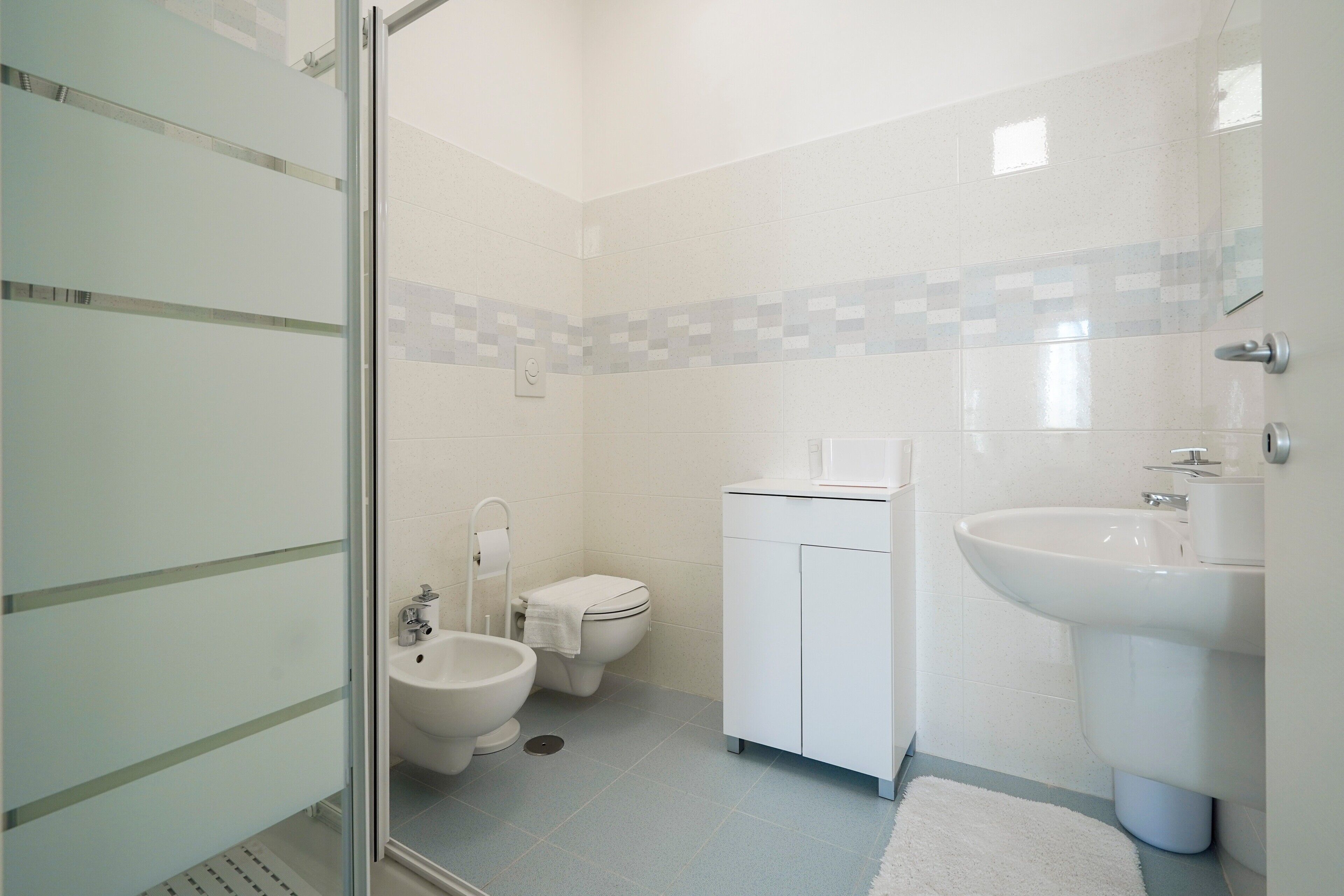 Ein Badezimmer mit Toilette, Bidet, Waschbecken und einer Duschkabine aus Glas.
