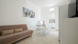 Un salon avec un canapé, une table à manger avec des chaises, un coin cuisine et un téléviseur.