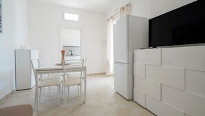 Une cuisine moderne avec des appareils électroménagers blancs, une table à manger avec des chaises et un grand téléviseur à écran plat fixé au mur.