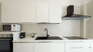 Une cuisine moderne avec des armoires blanches, un robinet noir, un four à micro-ondes, une cuisinière et un plan de travail noir.
