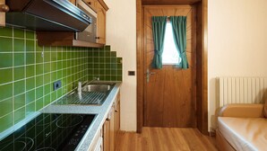 A compact kitchen with a stove, sink, and wooden cabinets. - Apartment "Casa San Marco N 1" with Mountain View, Garden & Wi-Fi (Livigno)