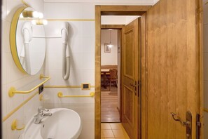 A bathroom with a white sink, a mirror, a hairdryer, and a wooden door.