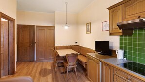 A kitchen with wooden cabinets, a dining table with chairs, a bench, a television, and a green tiled backsplash. - Apartment "Casa San Marco N 1" with Mountain View, Garden & Wi-Fi (Livigno)