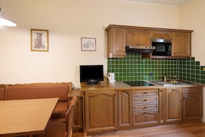 A kitchen with wooden cabinets, a microwave, a sink, and a television.