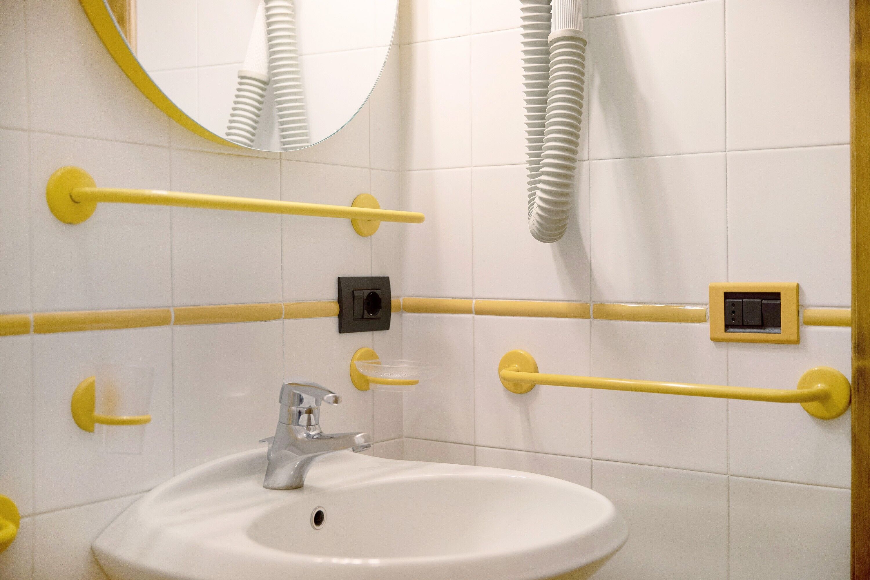 A bathroom with a white sink, yellow grab bars, a mirror, and a ventilation system.