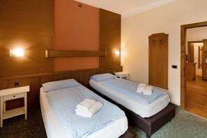 A hotel room with two single beds, a wooden wardrobe, a bedside table, and a mirror.