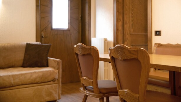 Ein Holztisch mit Stühlen, eine Holztür mit Fenster und ein beiges Sofa mit Kissen.