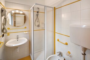 A bathroom with a white sink, mirror, and shower with yellow safety bars.