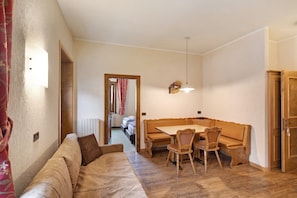 A cozy room with a sofa, a wooden dining table with chairs, a hanging light fixture, and a door.