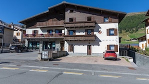Ein zweistöckiges Gebäude mit Balkon, einer Schilder mit der Aufschrift 'Banca Popolare di Sondrio' und einem roten Auto vor der Fassade.
