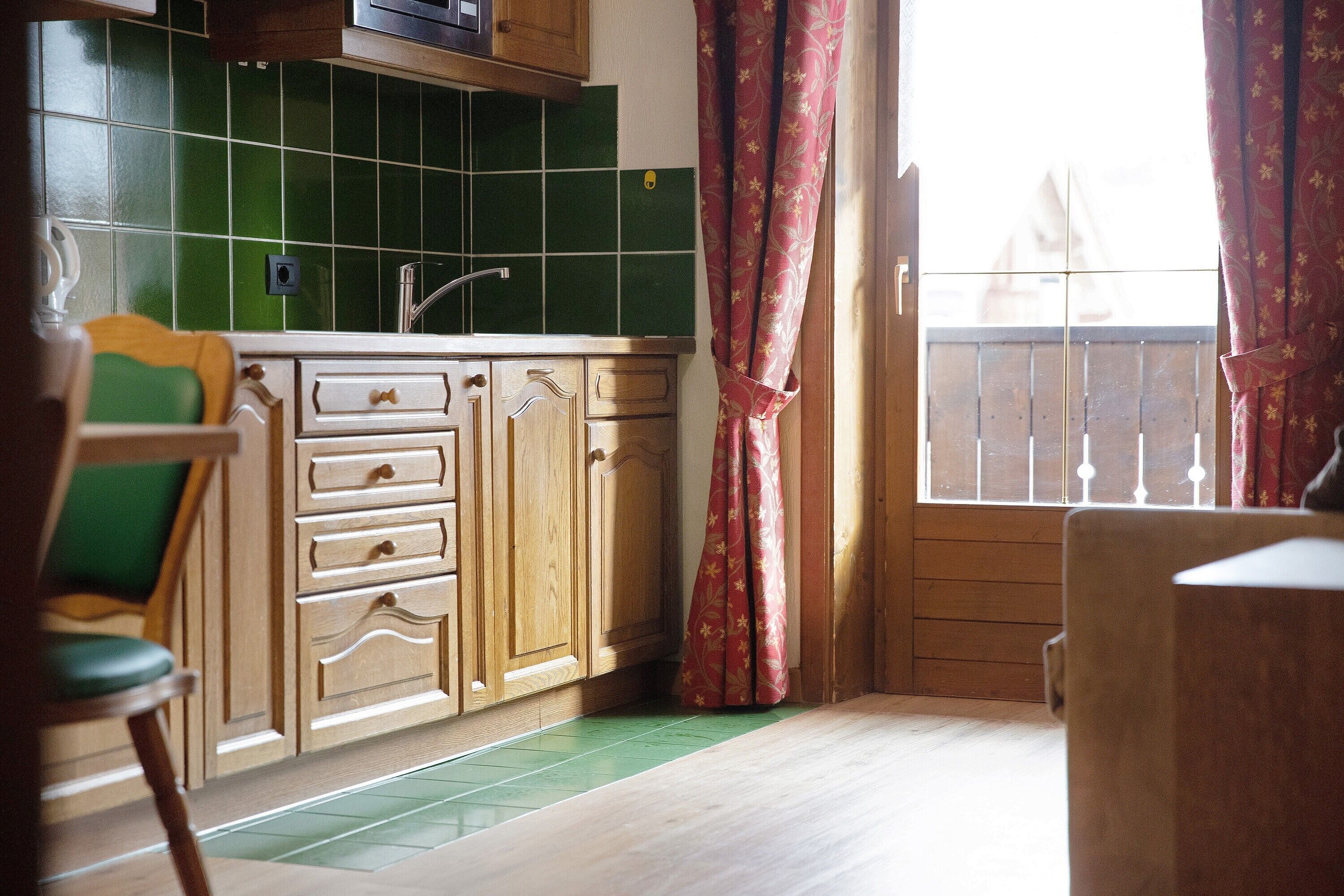A kitchen with wooden cabinets, a green tiled backsplash, and a window with a view.