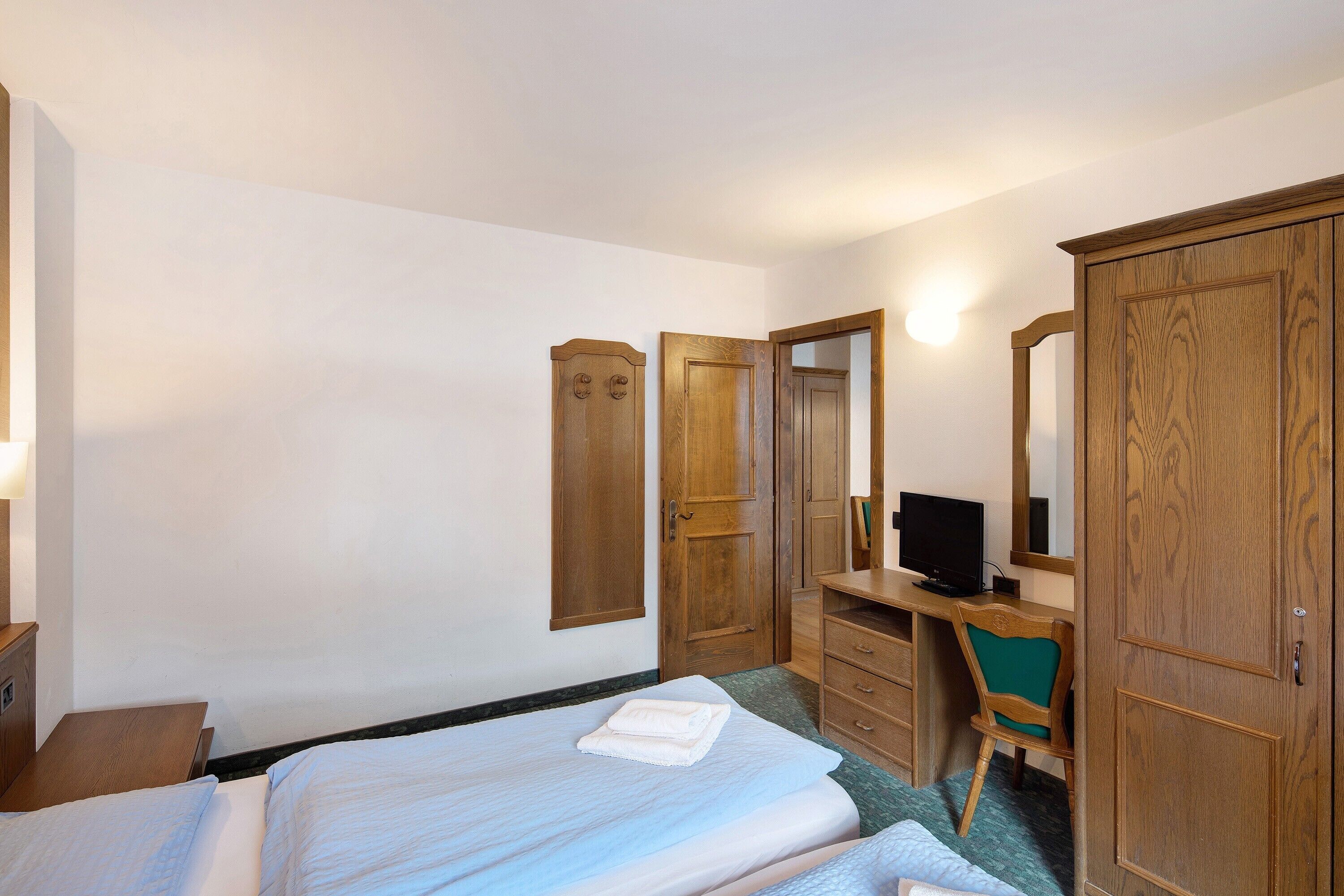 A hotel room with a bed, a desk with a computer, a chair, and wooden wardrobes.
