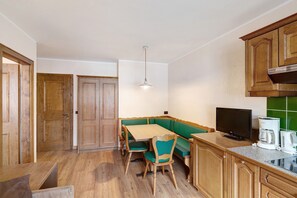 A compact kitchen with wooden cabinets, a dining table with chairs, a built-in bench, a television, and a coffee maker.