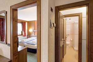 A hotel room with a bed, a bathroom with a shower, and a wooden door.