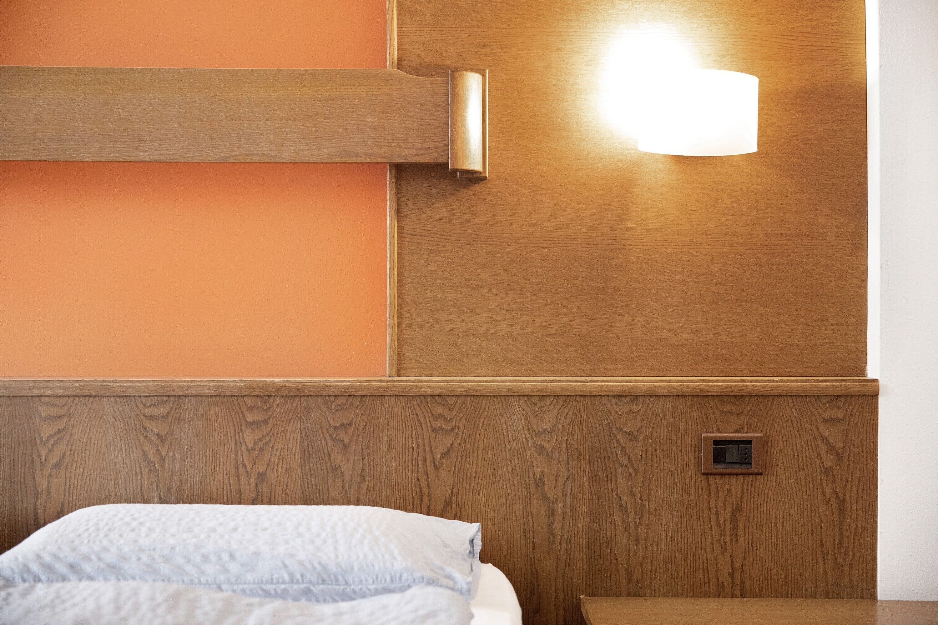 Habitació d'hotel amb un panell de fusta al capçal del llit, una taula de nit i una làmpada fixa a la paret.