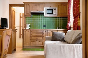 Une cuisine de taille réduite, dotée de meubles en bois, d’un four à micro-ondes et d’un dosseret de carrelage vert.