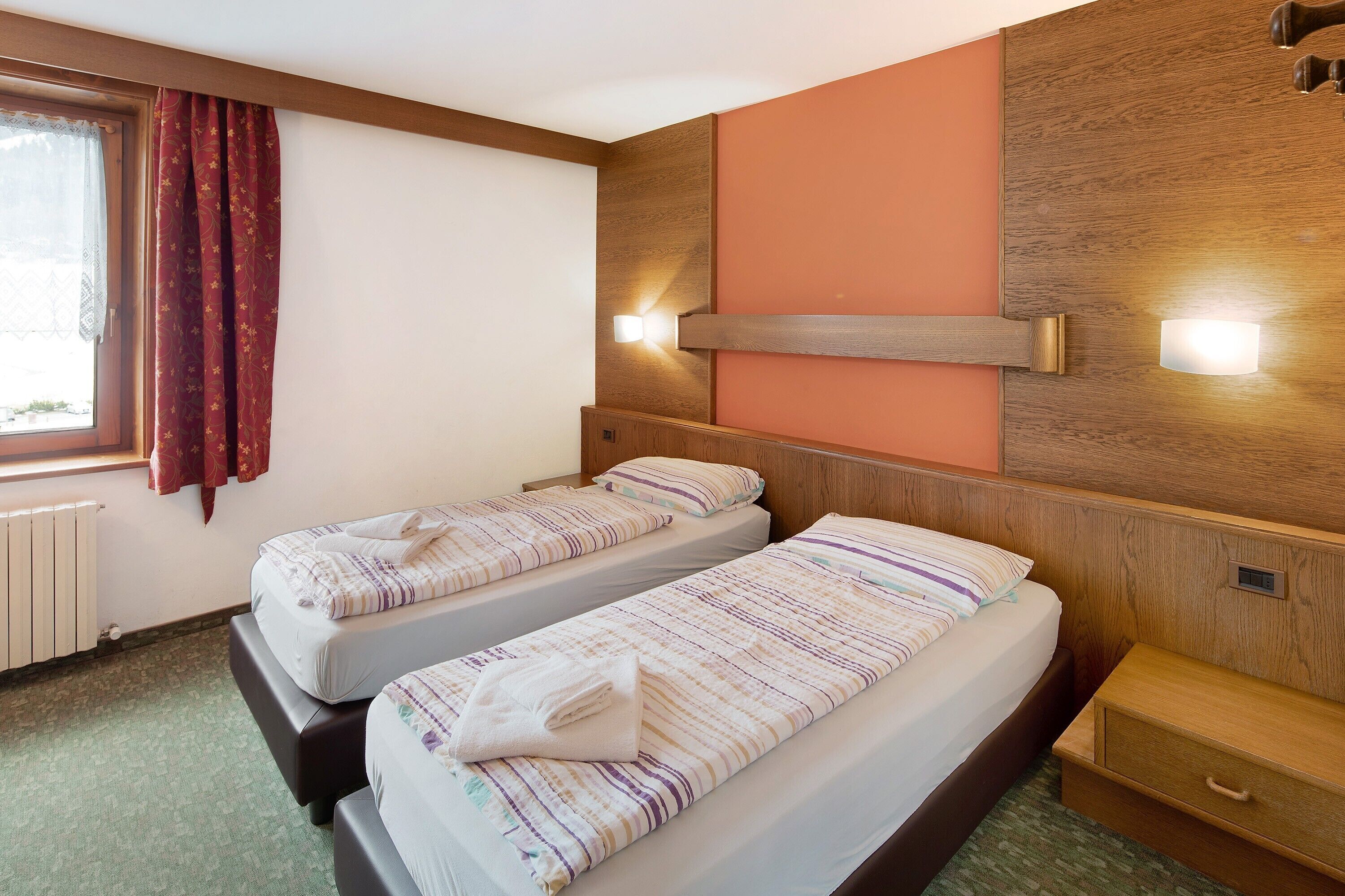 Une chambre d’hôtel avec deux lits, une fenêtre avec des rideaux, une tête de lit en bois et des lampes de chevet.