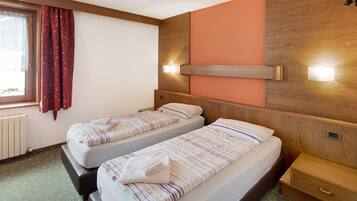 Une chambre d’hôtel avec deux lits, une fenêtre avec des rideaux, une tête de lit en bois et des lampes de chevet.
