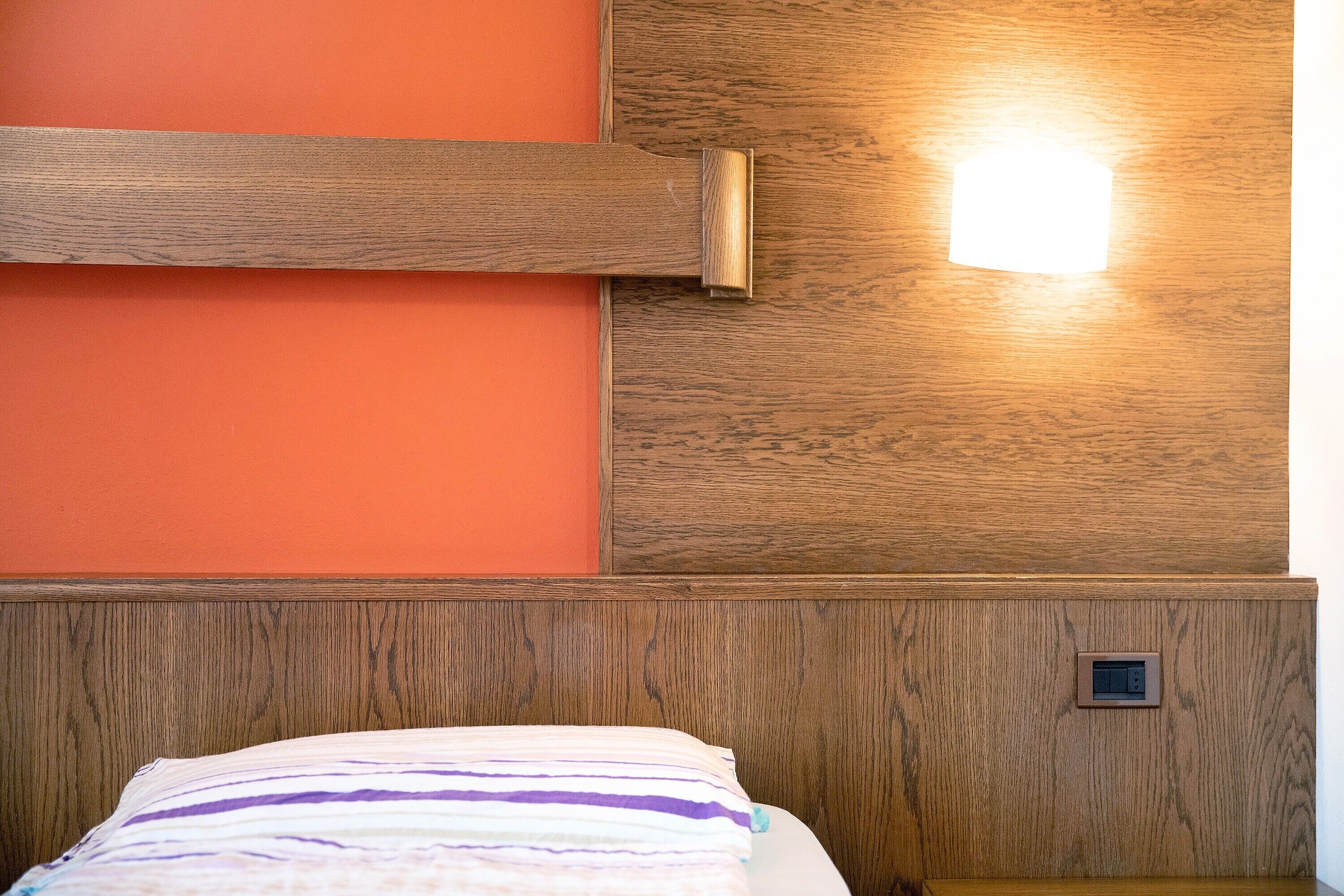 A room with a wooden headboard, a bed with a striped pillow, and a wall-mounted light fixture.