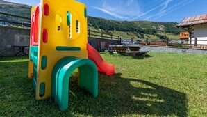 A playground with a slide and climbing structure in a grassy area with a mountain backdrop. - Holiday Apartment "Casa San Marco n 5" with Mountain View, Balcony & Wi-Fi (Livigno)