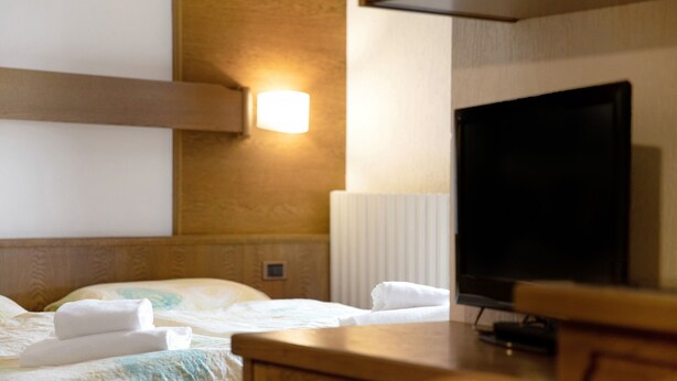 A hotel room with a bed, a television, and a wall-mounted light fixture. - Holiday Apartment "Casa San Marco n 6" with Mountain View, Balcony & Wi-Fi (Livigno)