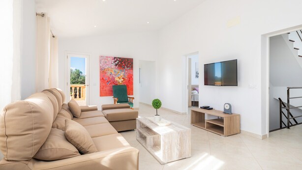 Ein modernes Wohnzimmer mit einem beigefarbenen Ecksofa, einem Couchtisch, einem Fernseher und einer Treppe.