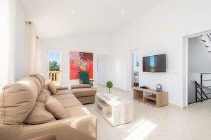 Una sala de estar moderna con un sofá seccional color beige, una mesa de centro, un televisor y una escalera.
