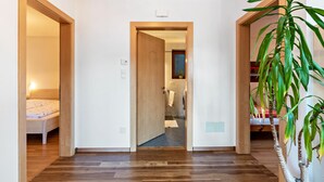 Een hal met houten vloer die leidt naar een slaapkamer met een bed en een badkamer met een handdoek.