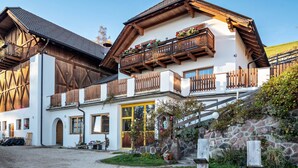 Een klassiek chalet met een houten balkon, een stenen muur en een grindpad.
