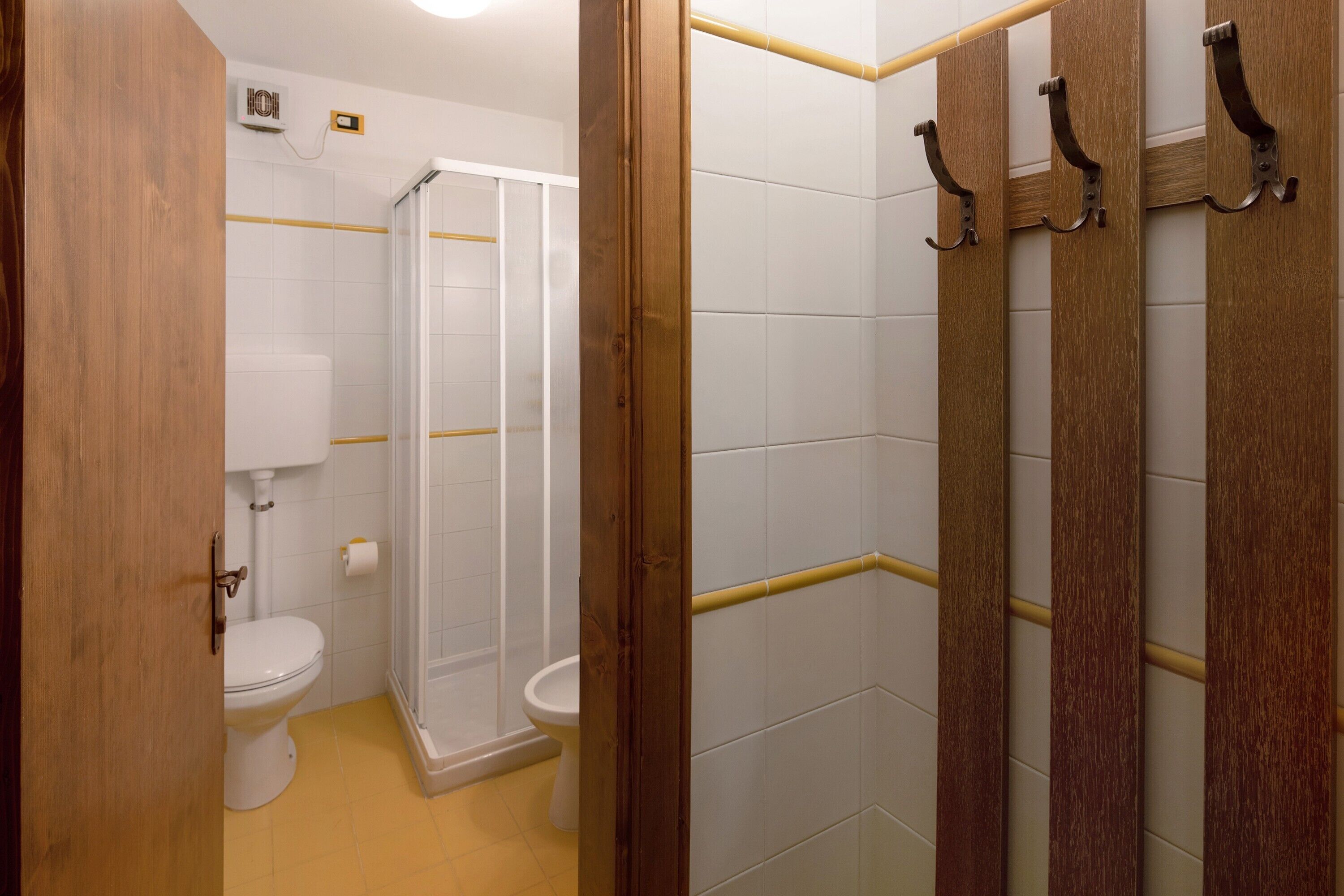 Ein Badezimmer mit Toilette, Dusche und einer Holztür mit Haken.