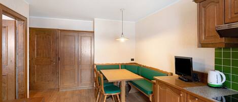 A compact kitchen with wooden cabinets, a green bench, a wooden table, and a kettle on the counter.