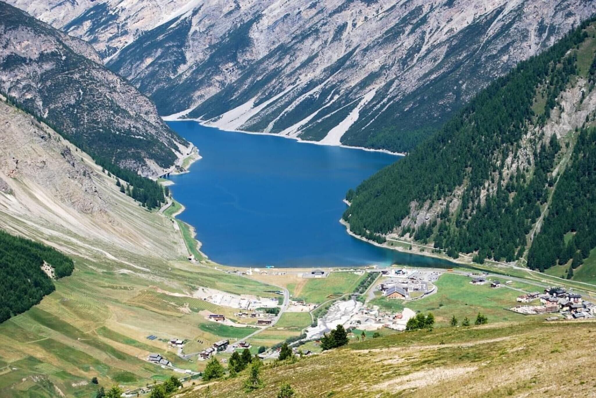 Paisagem montanhosa com um lago, um pequeno povoado com edifícios e uma estrada.