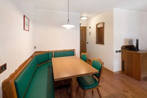 A dining area with a wooden table and green upholstered benches, a wooden cabinet, and a hanging light fixture.