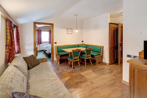 A living room with a sofa, a dining table with chairs, a wooden cabinet, and a television.