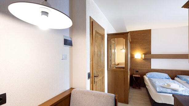 Ein Hotelzimmer mit einem hölzernen Bett, einem Stuhl, einem Schreibtisch und einer Tür zu einem weiteren Raum.