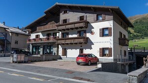 Ein zweigeschossiges Gebäude mit Balkon, davor ein rotes Auto und ein Schild mit der Aufschrift 'Banca Popolare di Sondrio'.