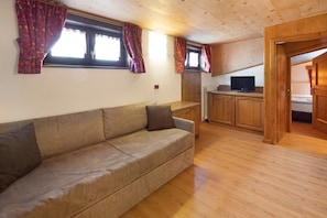 Une pièce au plancher de bois, avec un canapé, un téléviseur et un meuble.