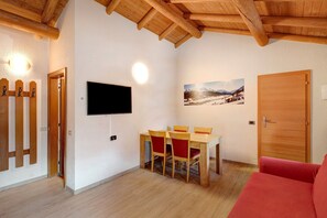 Una habitación con techo de madera, una mesa de comedor con sillas, un televisor de pantalla plana montado en la pared, una puerta y un cuadro en la pared.