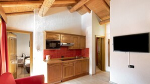 A compact kitchen with wooden cabinets, a built-in oven, and a flat-screen TV mounted on the wall. - Holiday Apartment "Casa Marcos n 29" with Mountain View, Balcony & Wi-Fi (Livigno)