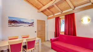 A room with a wooden ceiling, a red sofa, a dining table with chairs, and a wall-mounted light fixture. - Holiday Apartment "Casa Marcos n 29" with Mountain View, Balcony & Wi-Fi (Livigno)