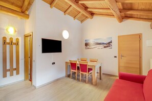 Una habitación con techo de madera, una mesa de comedor con sillas, un televisor de pantalla plana, una puerta y un sofá rojo.