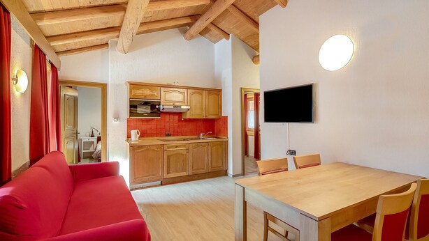 A cozy living room with a red sofa, wooden dining table, and kitchen in the background. - Holiday Apartment "Casa Marcos n 29" with Mountain View, Balcony & Wi-Fi (Livigno)